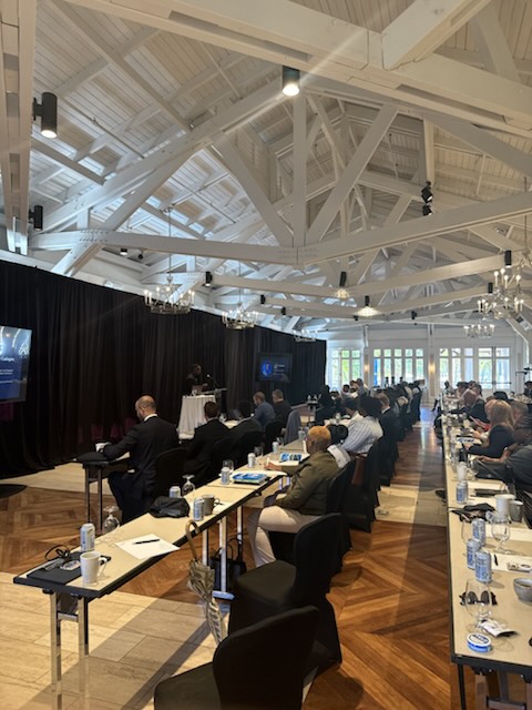 Attendees seated at long tables in the conference room